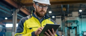 Engineer in hi-vis gear reviewing real-time machine data on a tablet on the factory floor, illustrating the shift to machine-truth monitoring featured at IMTS 2026
