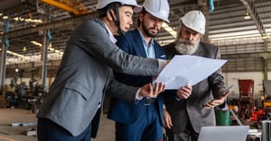 Three engineers reviewing drawings together on a factory floor, representing running the whole operation on one platform.