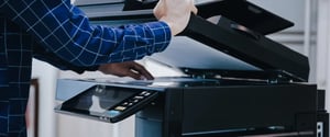 Worker scanning a stack of documents at an office multifunction scanner, the Mass Scanning workflow Doc-Trak automates with AI